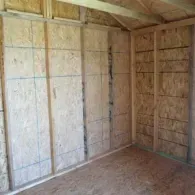 An interior view of a wooden shed with oriented strand board (OSB) walls and floor under a sloped roof.