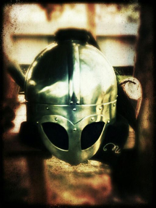 Close-up of a metallic medieval helmet with eye slits, centered against a blurred, warm-toned background