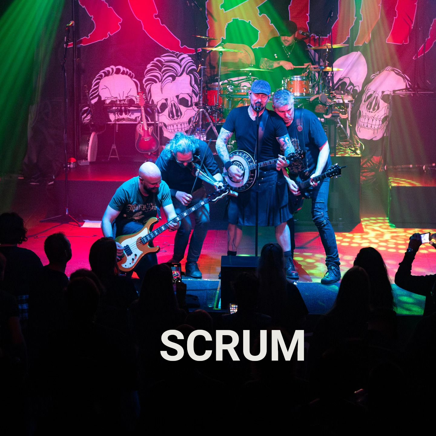 De band SCUM treedt op het podium op en speelt instrumenten voor een publiek. Groene en rode verlichting.