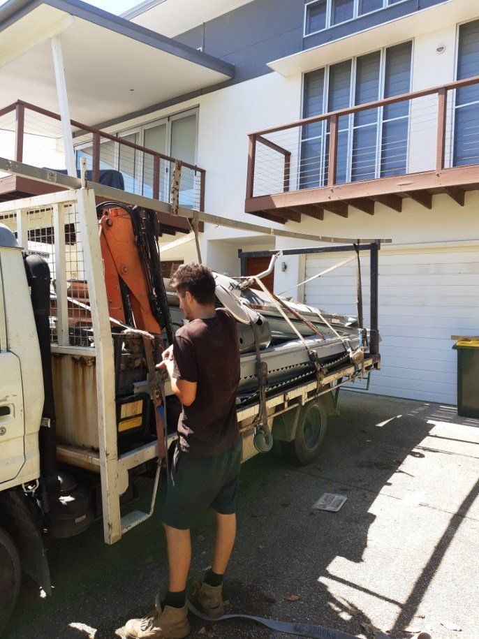 A Man Is Standing Next To A Truck In Front Of A House — East Coast Metal Recycling In Tugun, QLD