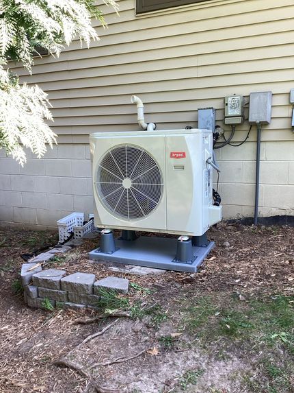 A man is working on an air conditioner outside of a building while holding a clipboard.