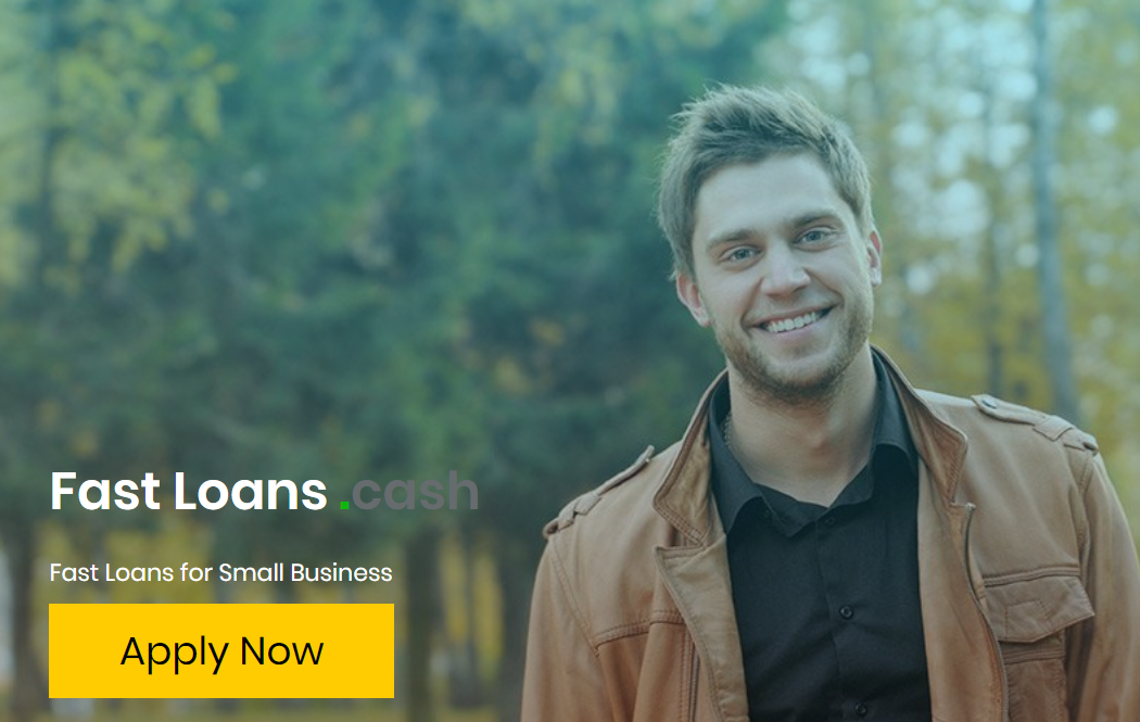 A man in a brown jacket is smiling in front of a forest.