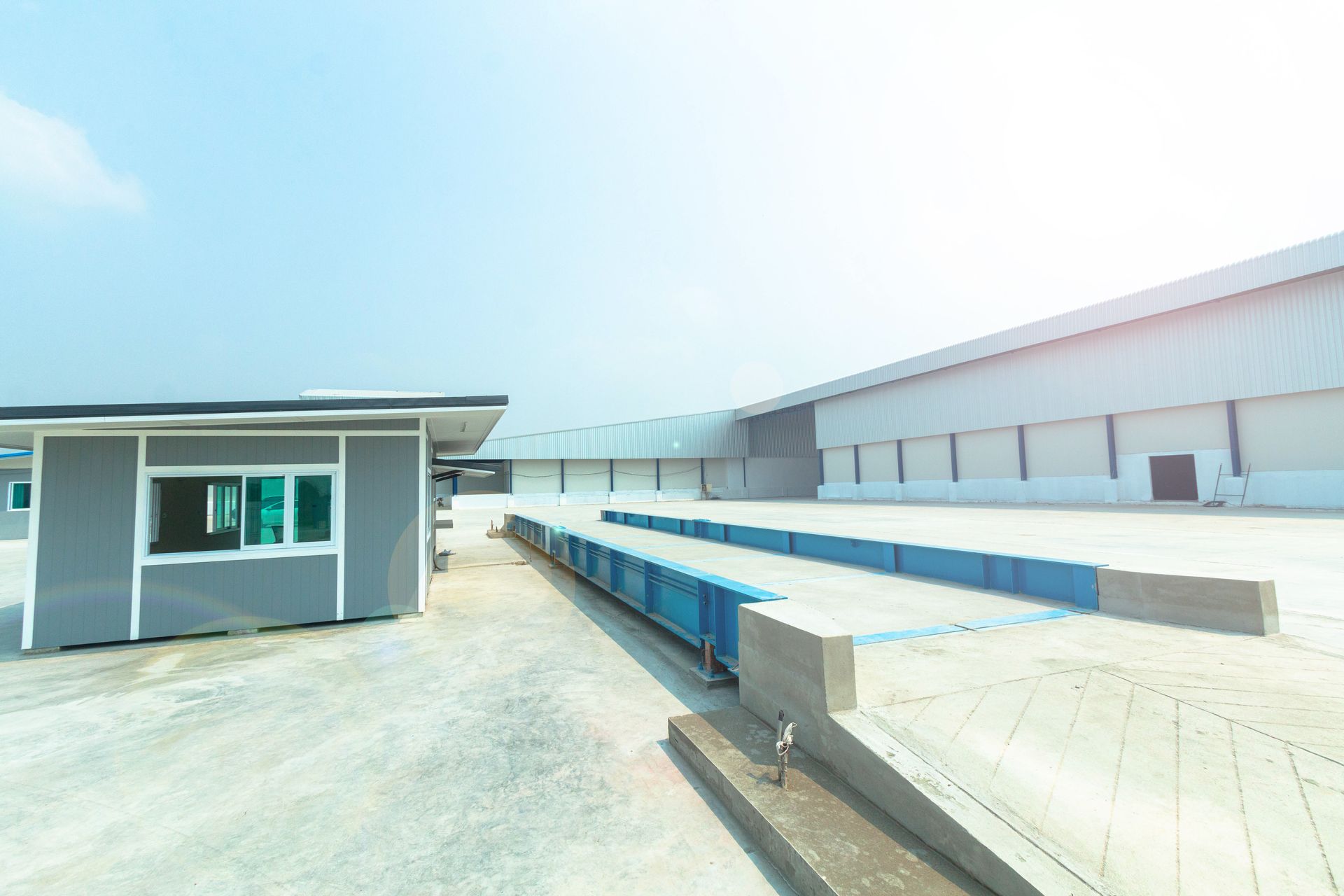 A long truck scale platform sits beside a small control building on a bright day.