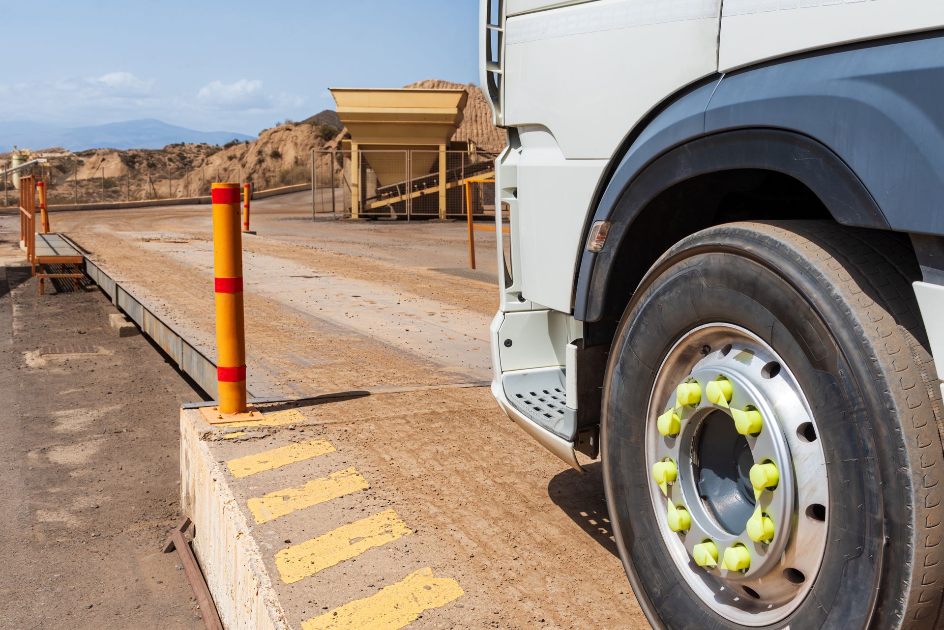 A truck pulls onto a metal scale platform at a dusty industrial site. A truck pulls onto a metal scale platform at a dusty industrial site.