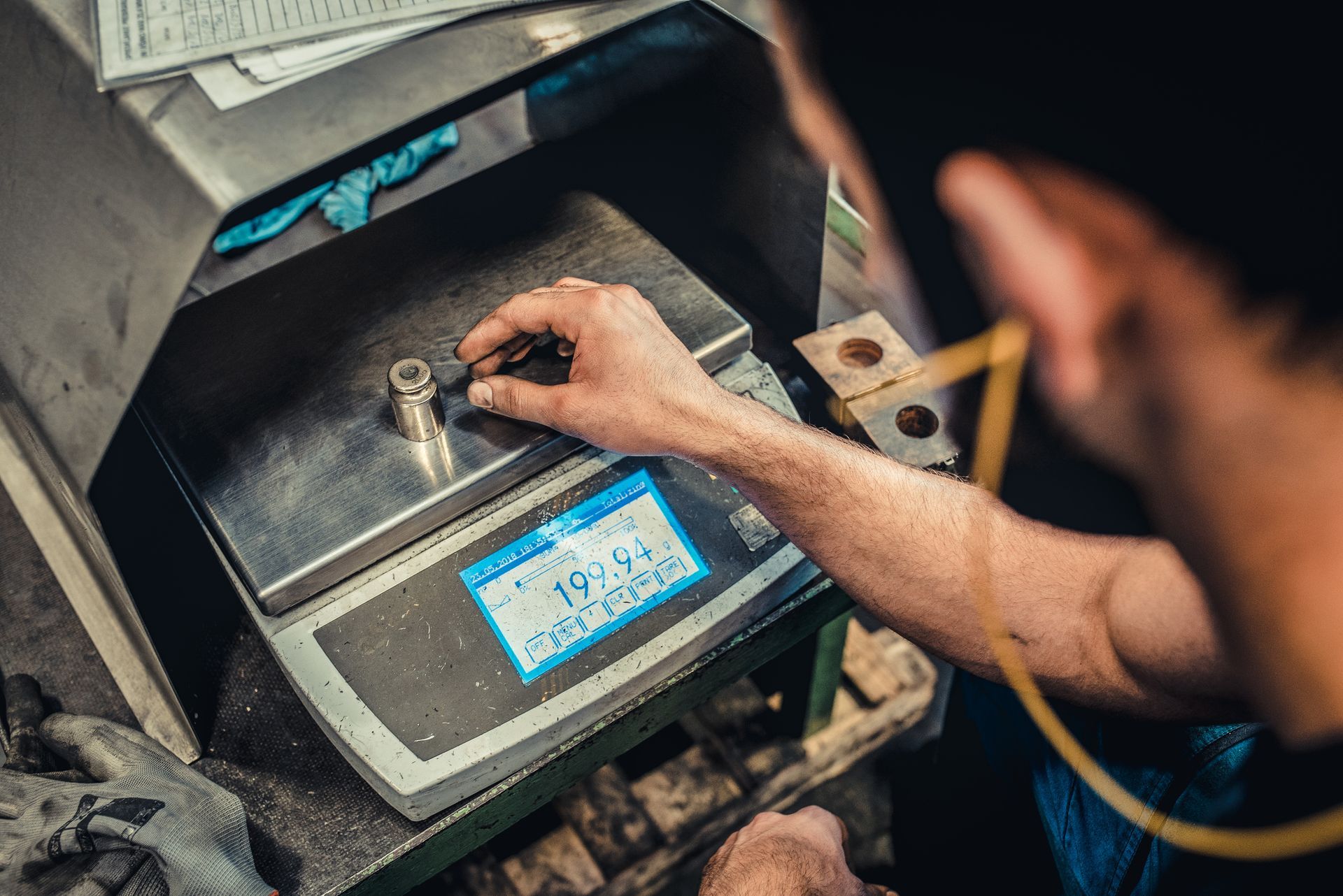 Man weighting a metal piece on an electronic balance provided by an industrial scale supplier.