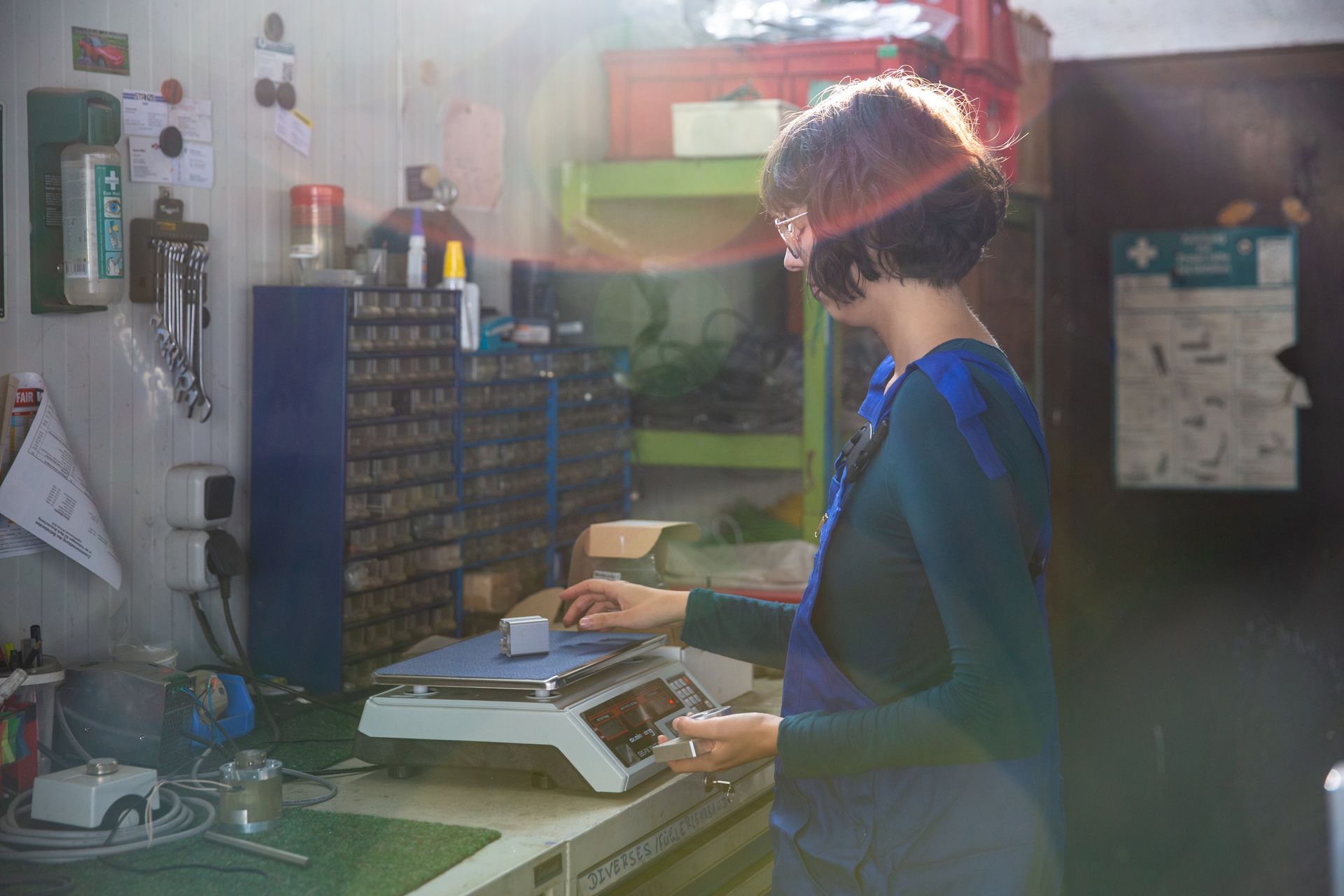 A young female technician weighs metal parts on a scale.