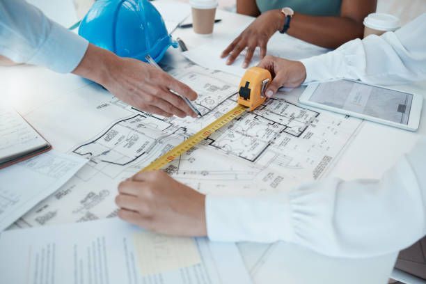 Engineers reviewing blueprints with tape measure, planning with trusted floor scale supplier.