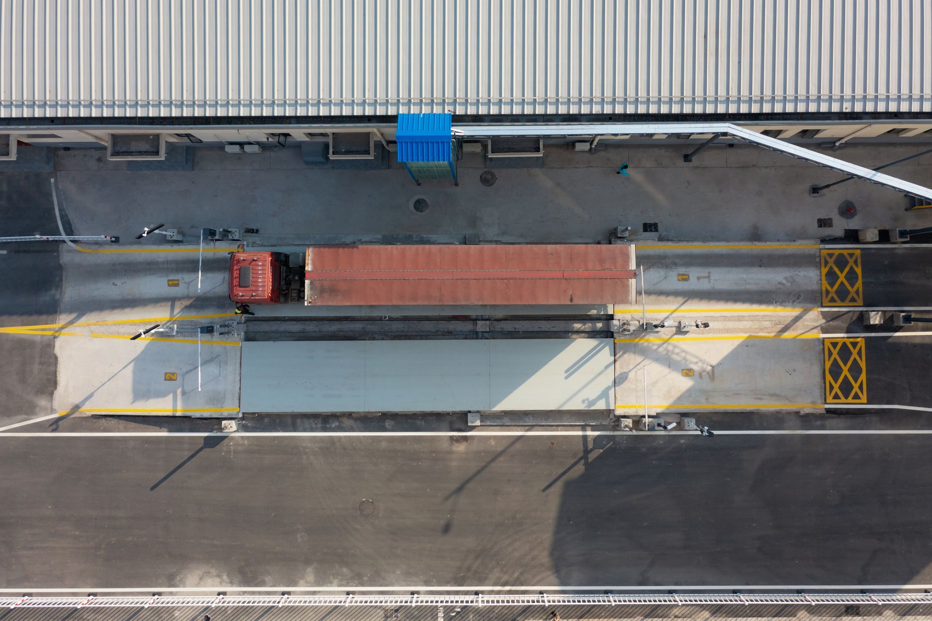 Aerial view of a red truck on a scale next to a building with marked weighing zones. Aerial view of a red truck on a scale next to a building with marked weighing zones.