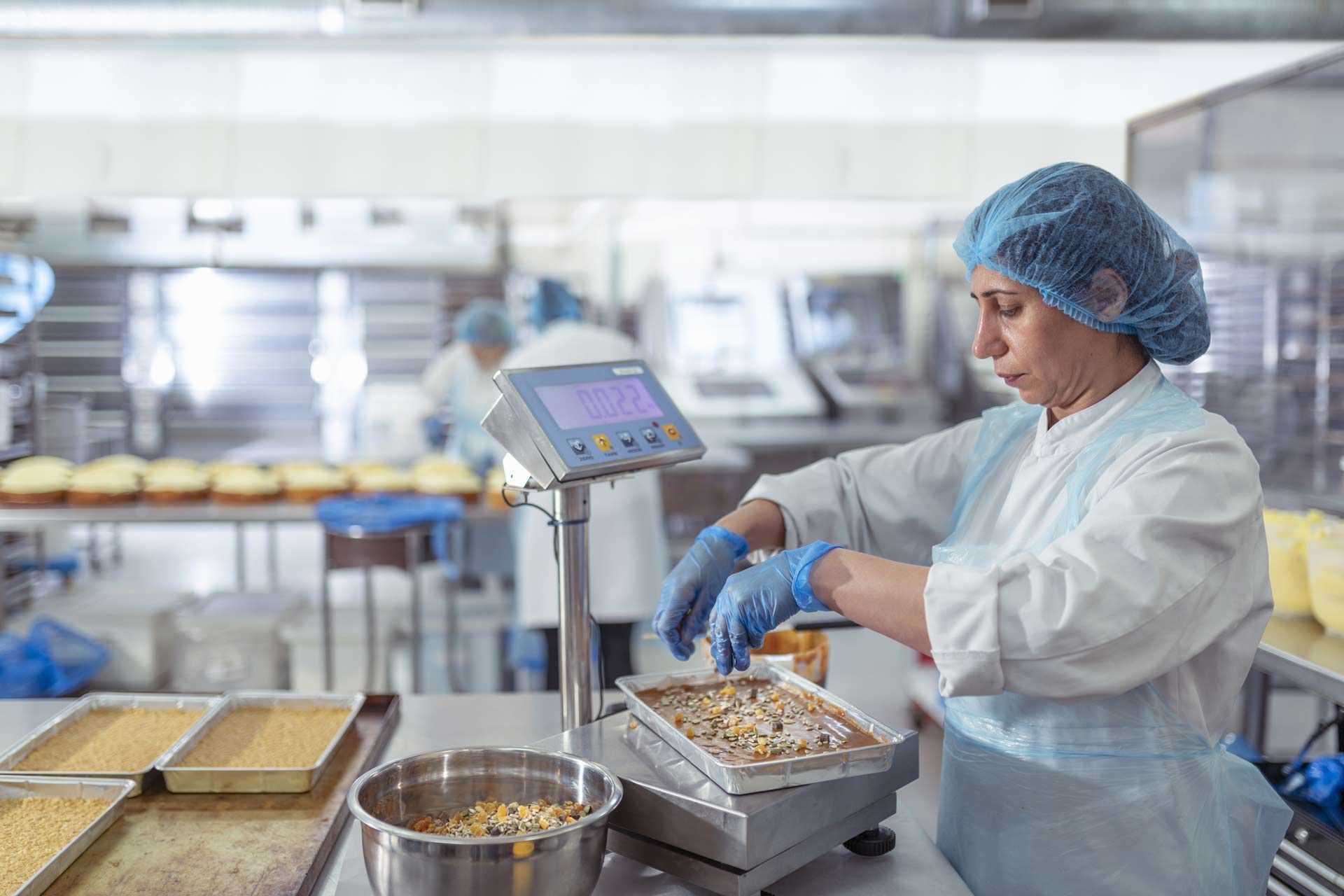 Female worker spreading nuts onto a bake tray on a scale.