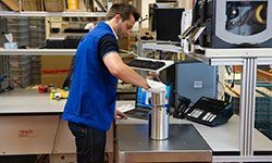 A man in a blue vest is standing at a counter in a factory.