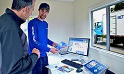 Two men are shaking hands in front of a computer in a room.