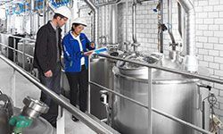 A man and a woman are standing in a factory looking at a clipboard.
