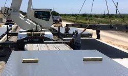 A crane is lifting a large piece of metal on top of a truck.