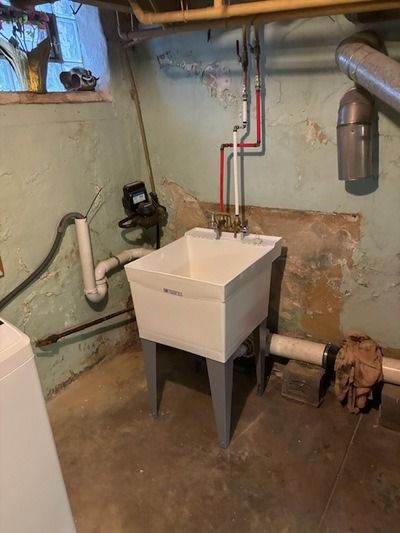 Laundry sink in a basement. White utility sink with gray legs, pipes on walls.