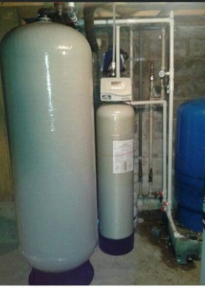 Water filtration system with large white tanks and a control panel in a basement setting.