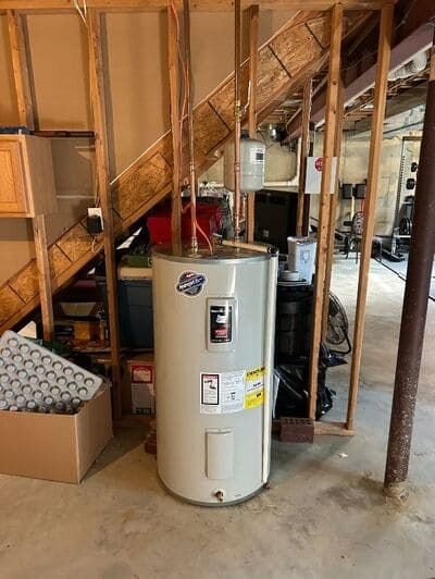 Water heater in a basement, near stairs and a wooden frame.