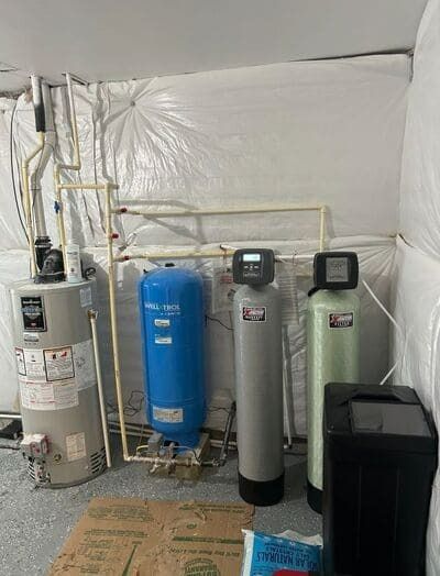 Water heater and water filtration system in a utility room. Pipes and tanks are visible.