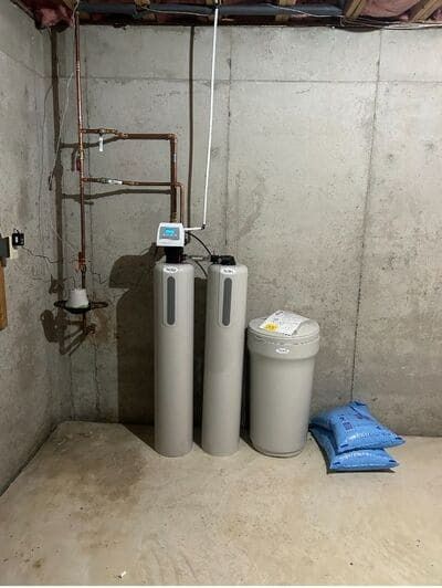Water softener system in a basement setting with concrete walls and bags of salt.