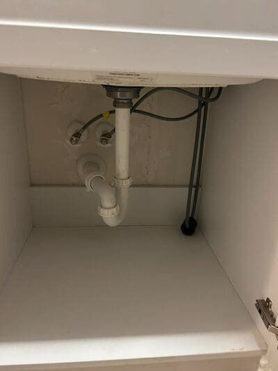 White bathroom sink plumbing under a cabinet: drainpipe, p-trap, water supply lines.