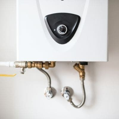 White water heater mounted on a wall, with pipes and valves visible below.