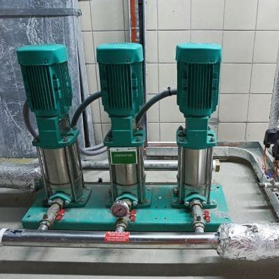 Three green industrial water pumps on a metal base with piping in an industrial setting.