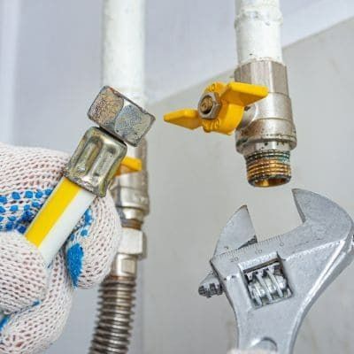 Gloved hand with wrench loosening gas line fitting near yellow valve.