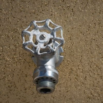 Metal water spigot with white, spoked handle against a textured, tan wall.