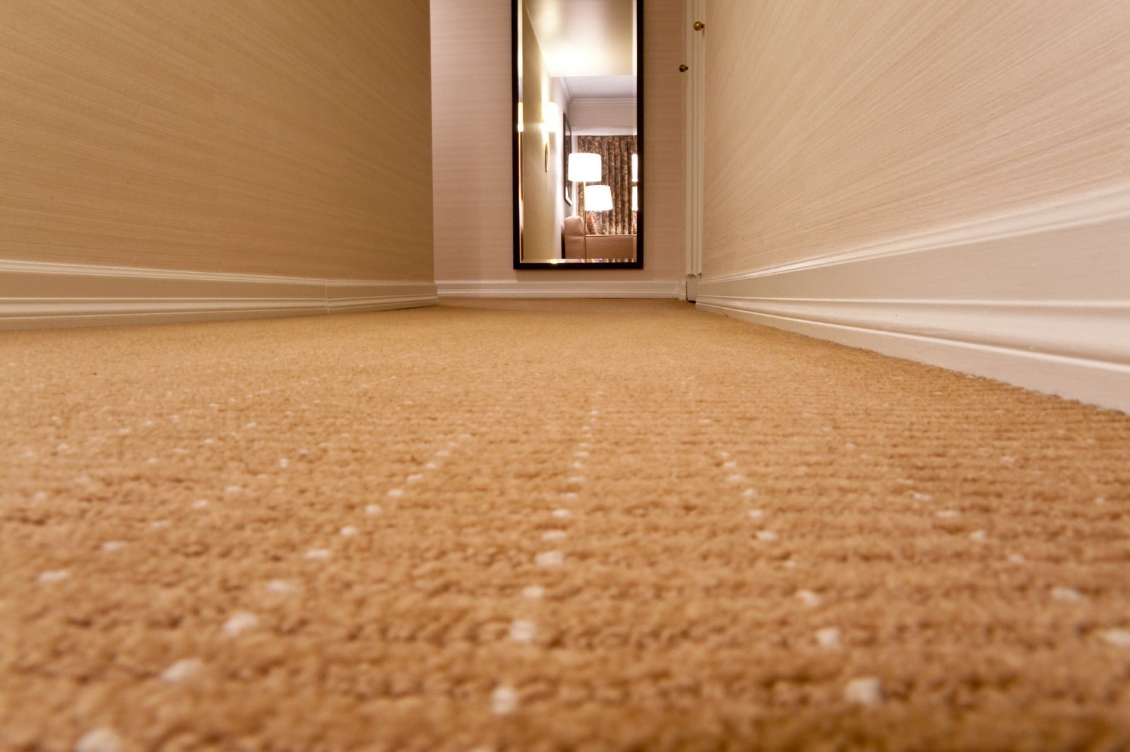 A hallway with a carpeted floor and a mirror on the wall.