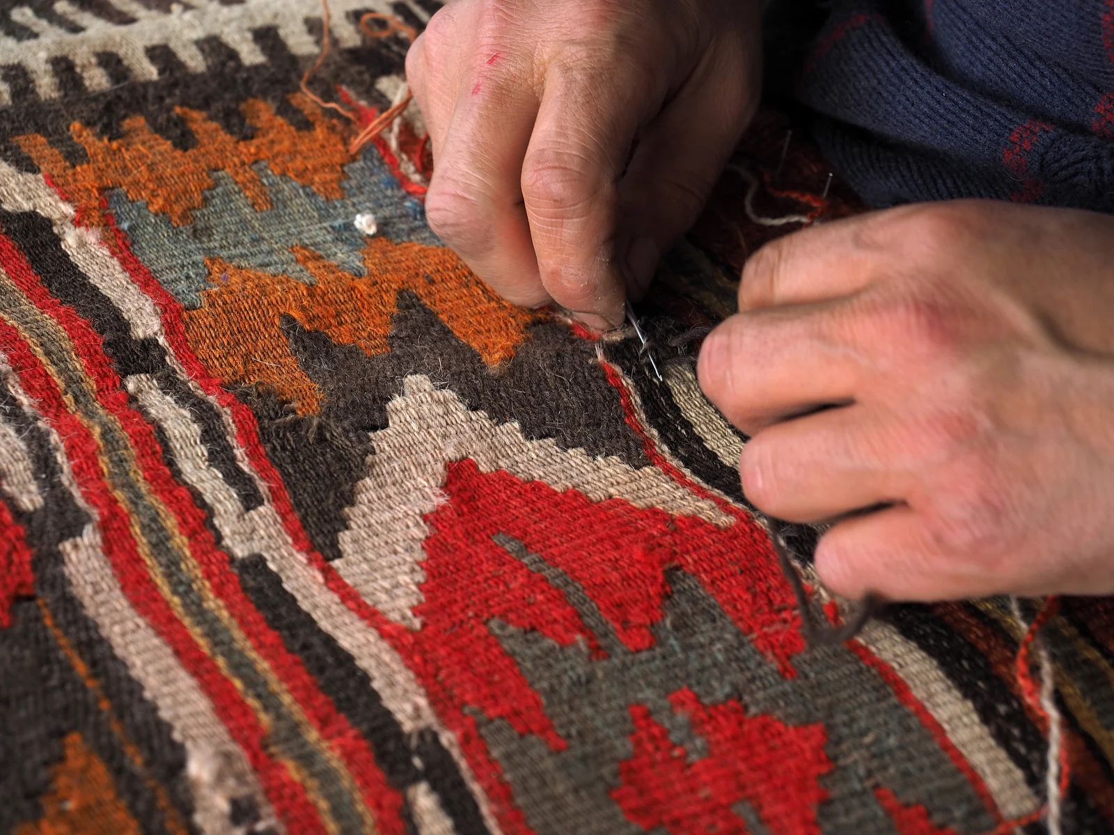 Hands sewing a colorful, patterned rug, detail view.
