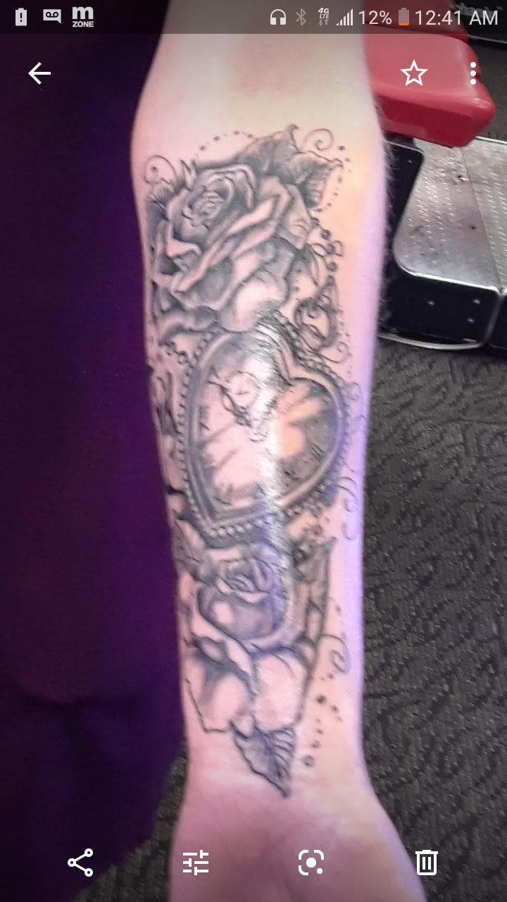 A person has a tattoo on their forearm with roses and a heart