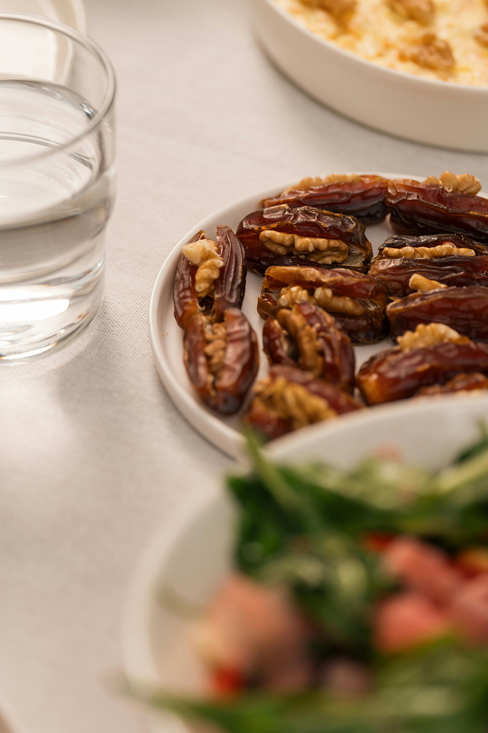 Plate of stuffed dates with walnuts, a glass of water, and a side dish on a white tablecloth.