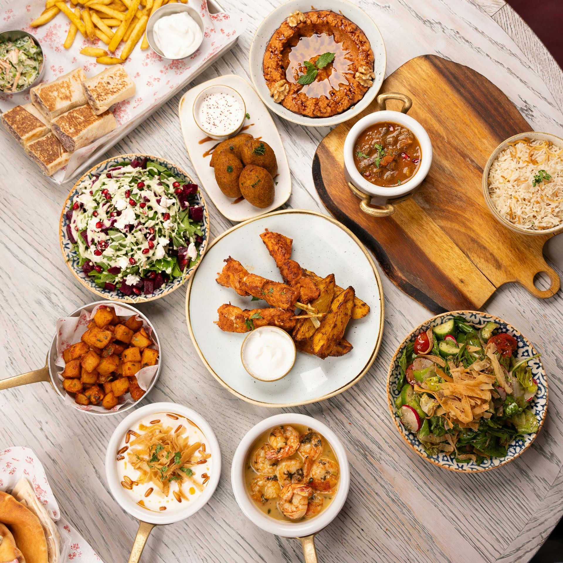 Overhead shot of a table laden with Middle Eastern food: salads, dips, falafel, fries, and rice.