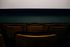 Rows of empty, worn, gold theater seats facing a blank, white screen. Dark, muted interior setting.