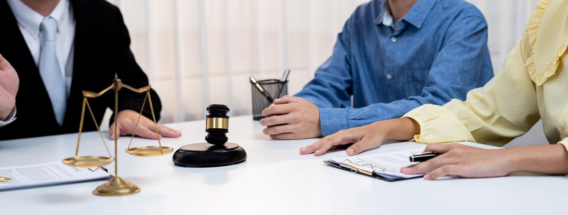 Una persona in abito elegante, una persona con una camicia blu e una persona in giallo siedono a un tavolo con il martelletto e la bilancia del giudice.