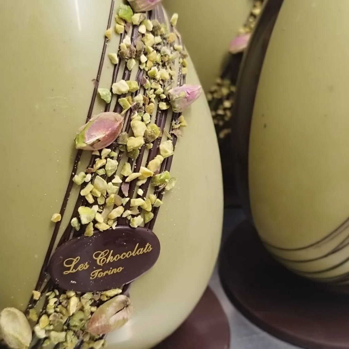 Uova di Pasqua di cioccolato verde con glassa di cioccolato fondente, pistacchi e il logo Les Chocolats Torino.