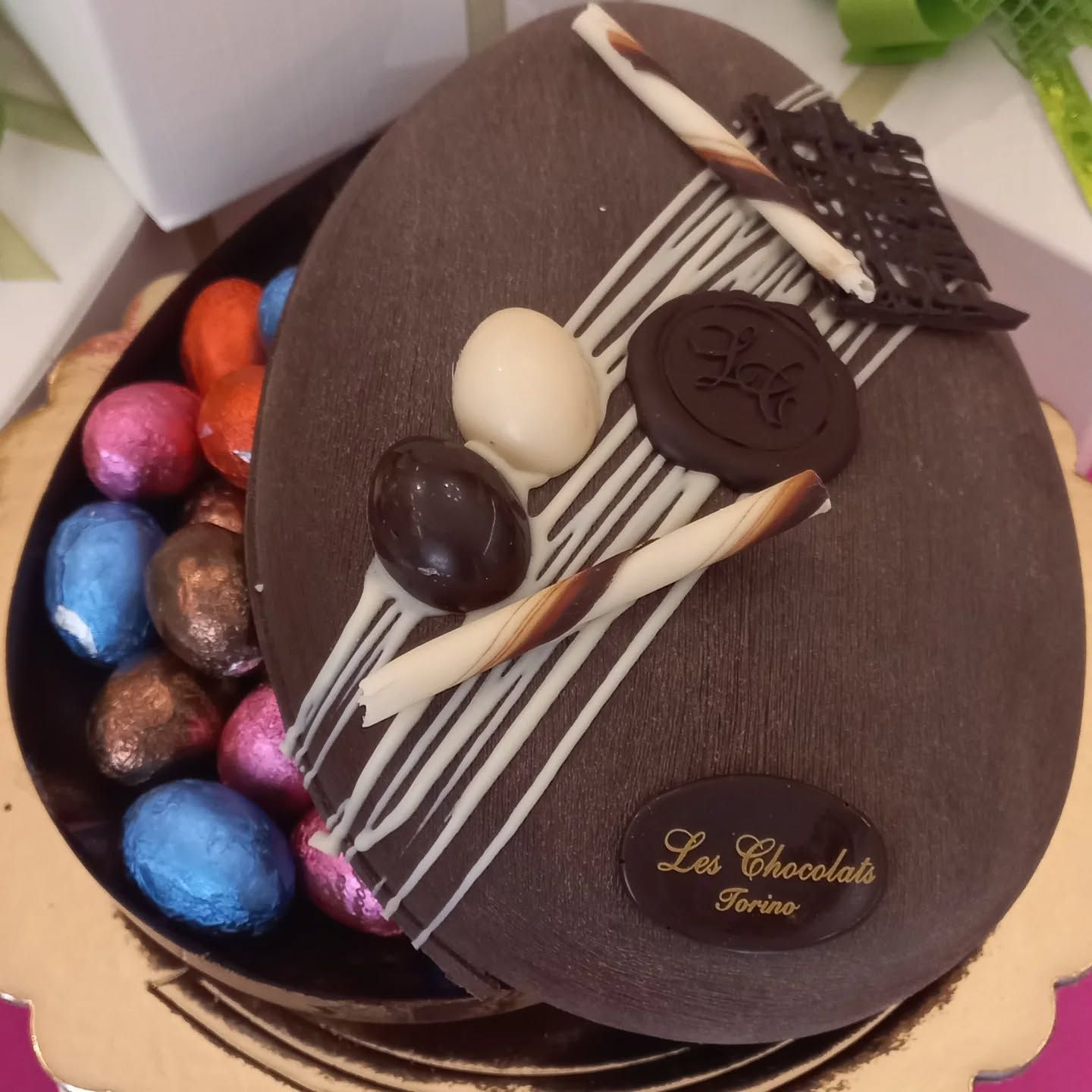 Uovo di Pasqua di cioccolato fondente, ripieno di caramelle avvolte in carta stagnola, decorato con strisce bianche e pezzetti di cioccolato.