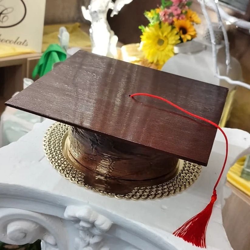 Torta di laurea al cioccolato con nappa rossa, esposta su un piedistallo bianco.