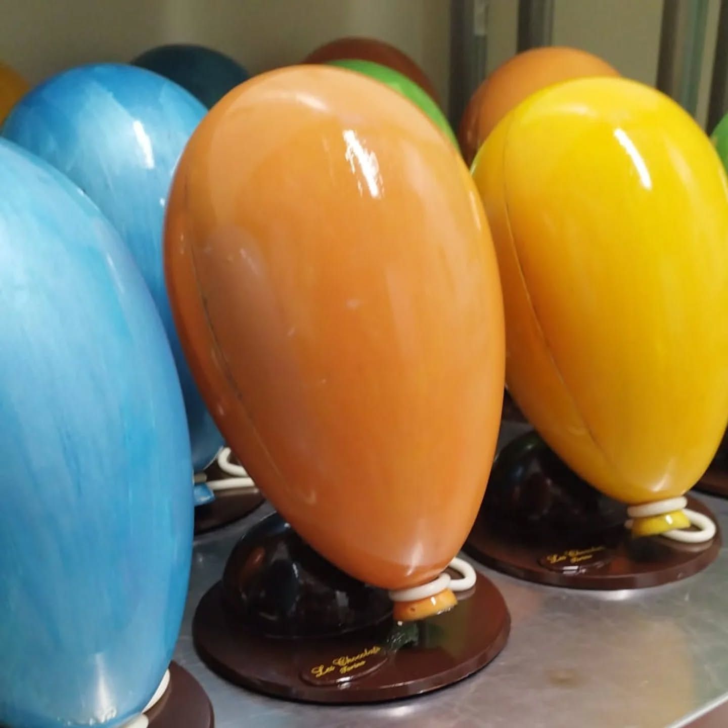Dolci colorati a forma di palloncino, glassati di arancione e giallo, su base di cioccolato.