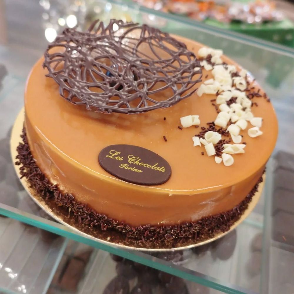 Torta glassata al caramello con decorazioni di cioccolato, logo e pezzetti di cioccolato bianco.