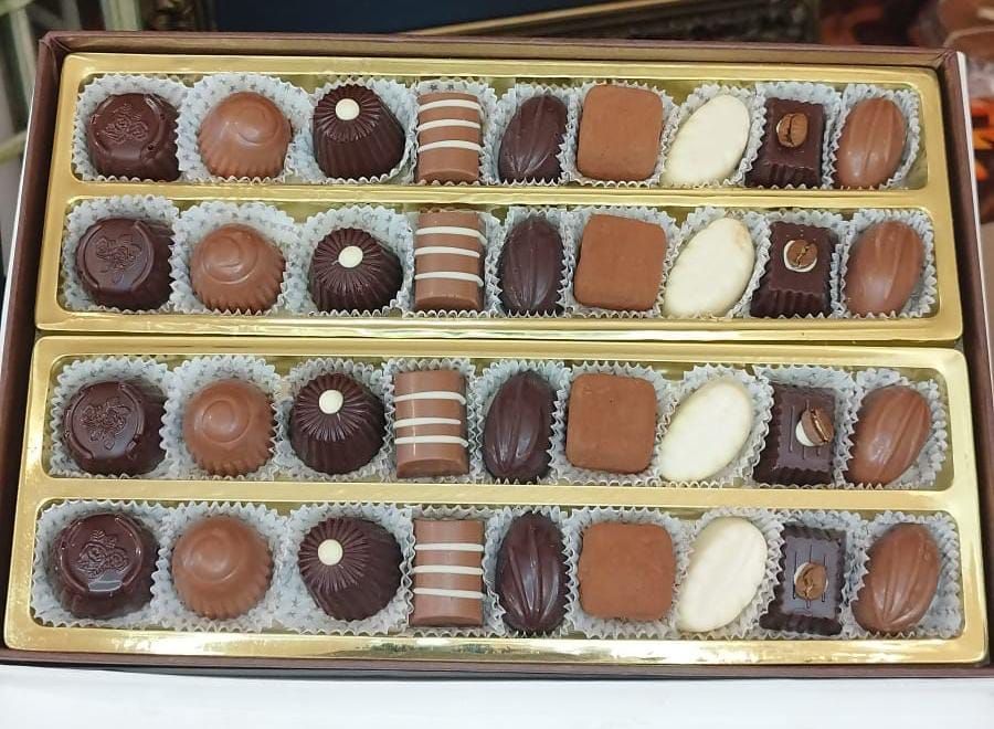 Primo piano di una scatola di cioccolatini assortiti, di varie forme e colori chiari e scuri.