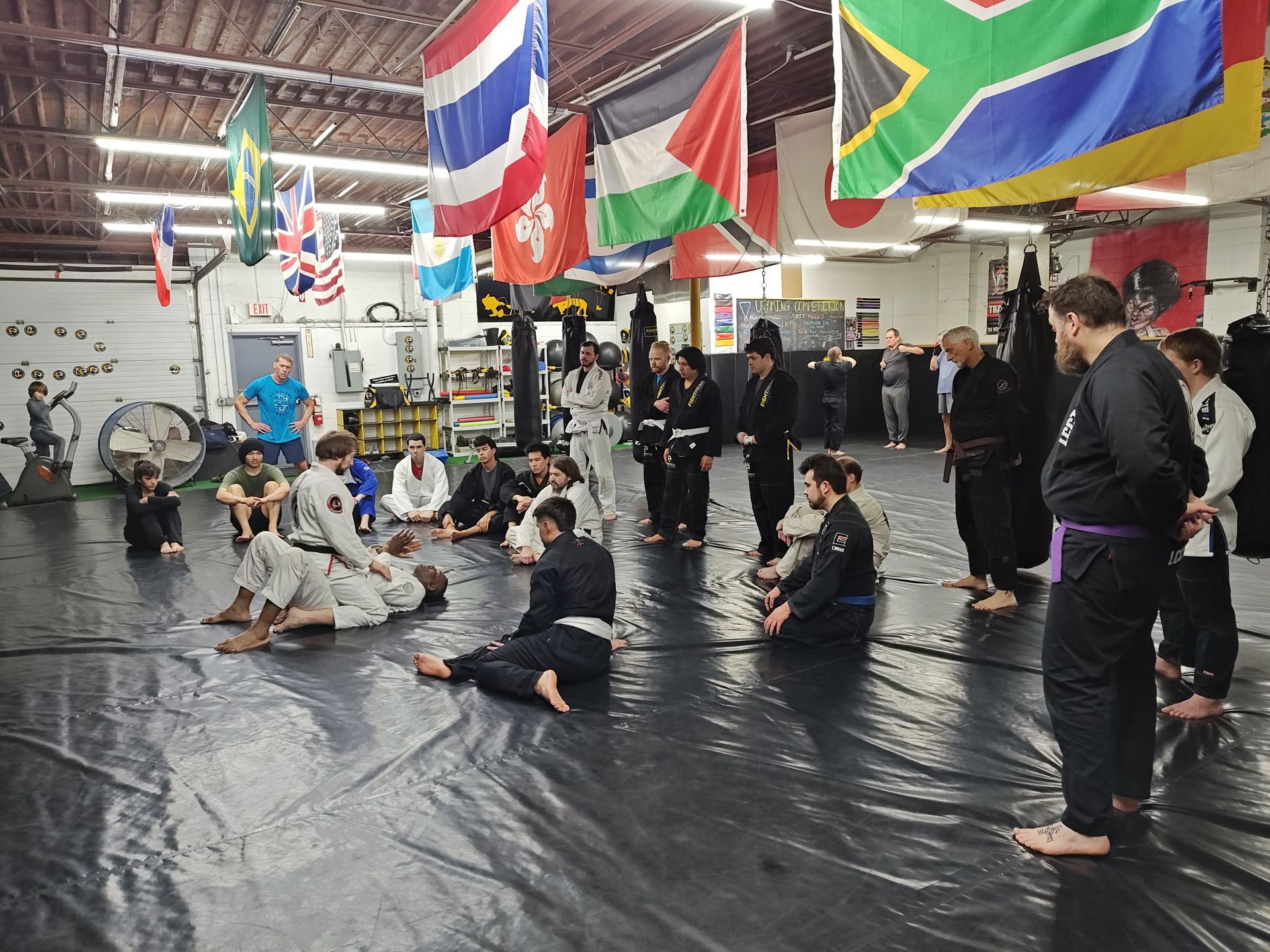 A group of people are sitting on a mat in a gym with flags hanging from the ceiling.