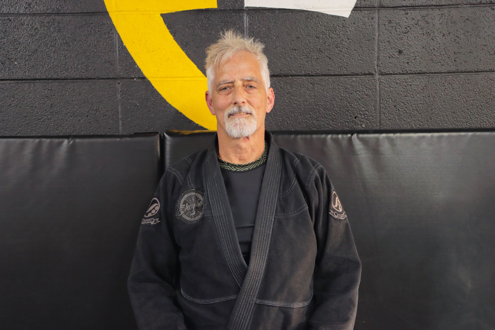 A man in a black karate uniform is standing in front of a wall.