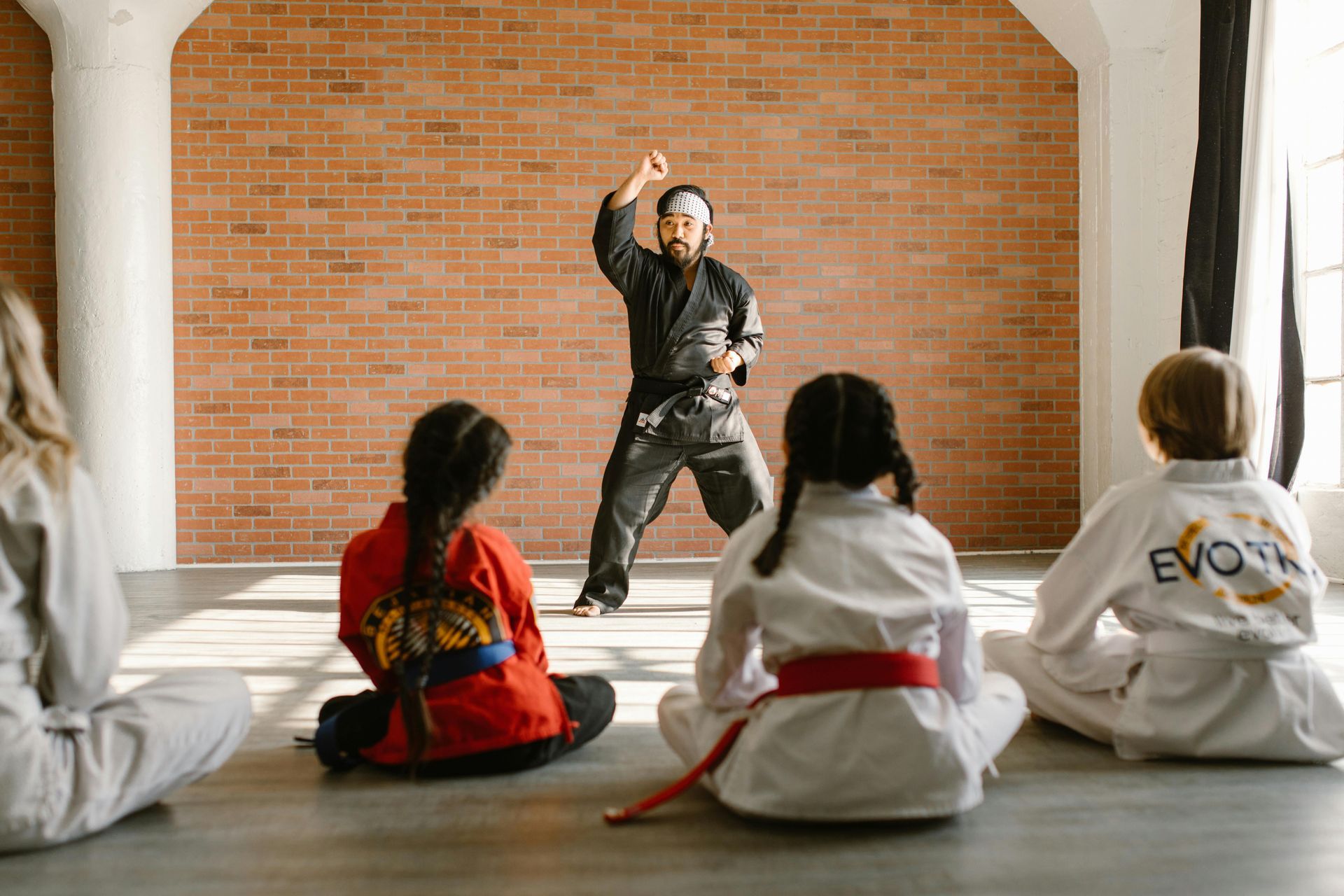 Karate instructor demonstrating a move for students, who sit on the floor, in a studio.