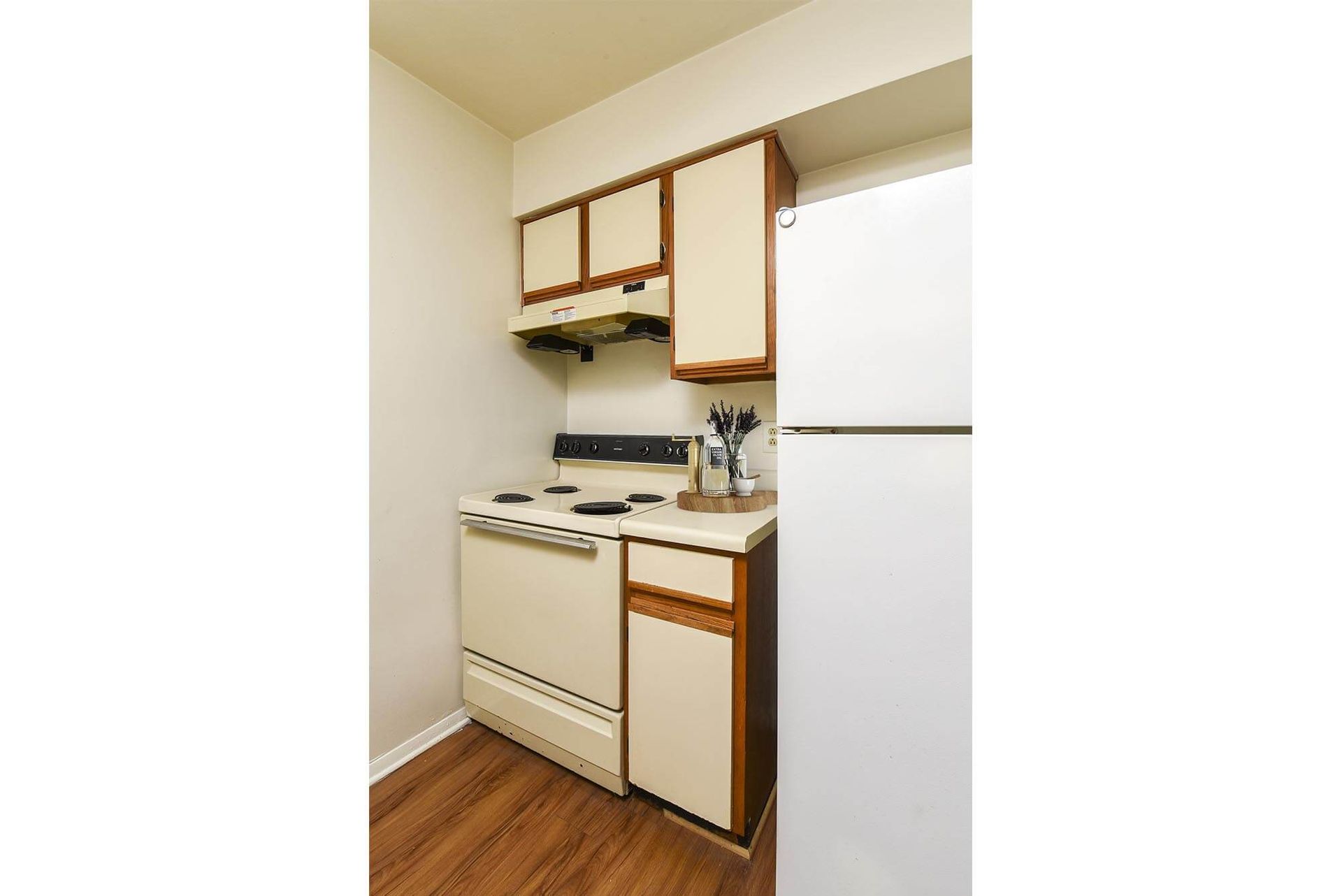 Compact apartment kitchen with a white stove, cabinets, and a fridge.