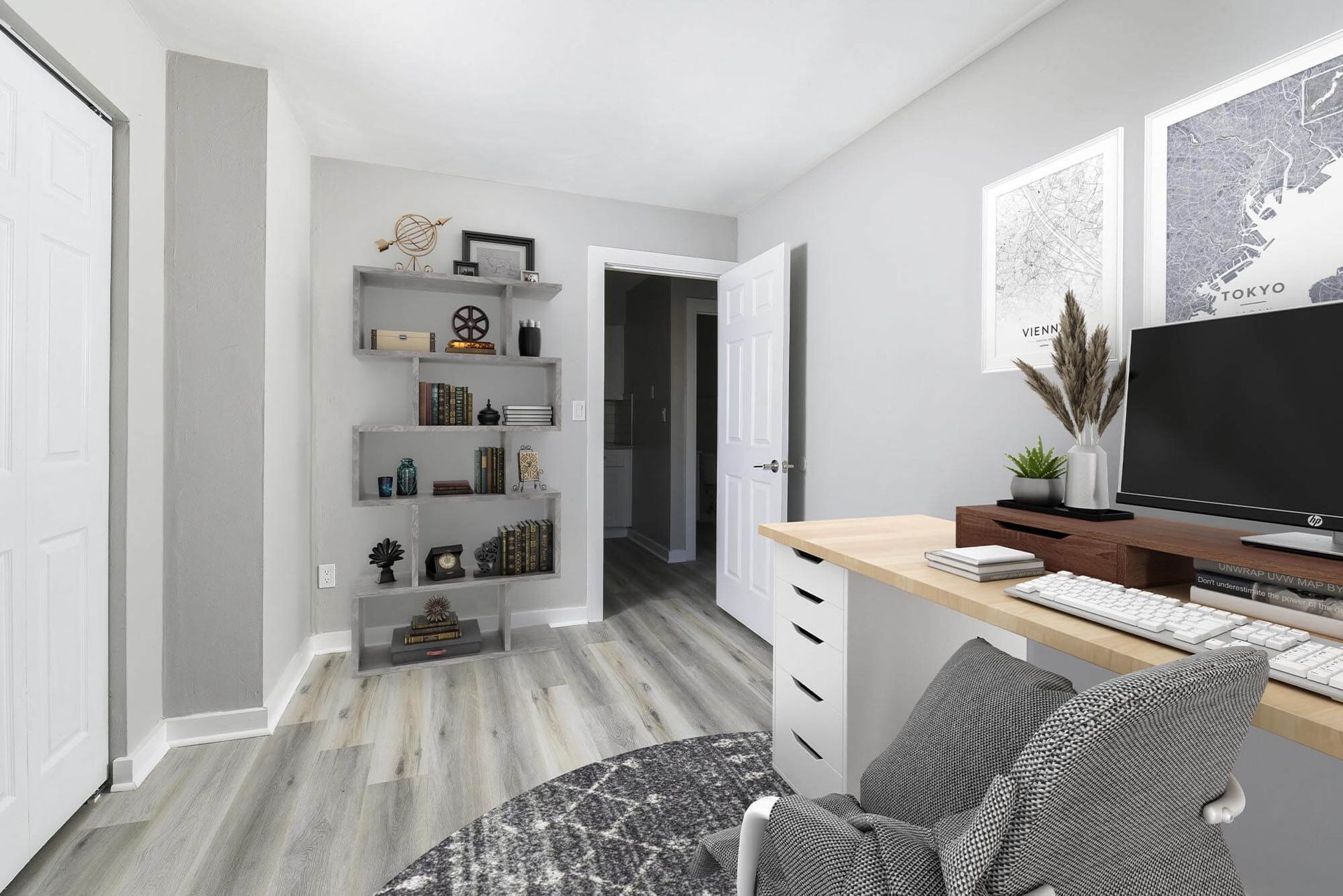 Home office setup with a wooden desk, monitor, and gray shelving in a light-gray apartment room.