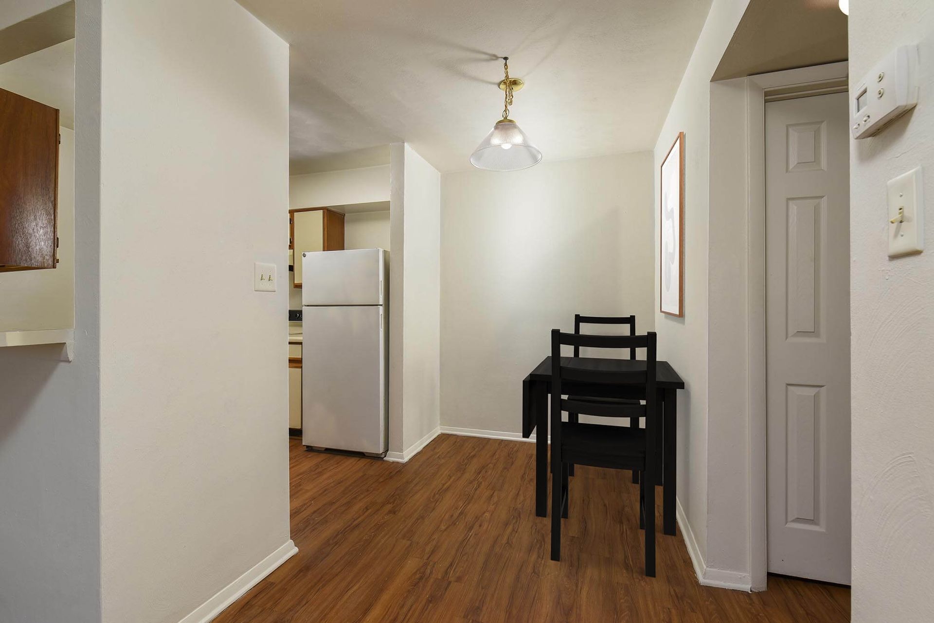 Dining area with a black table and two chairs adjacent to a small kitchen and refrigerator.