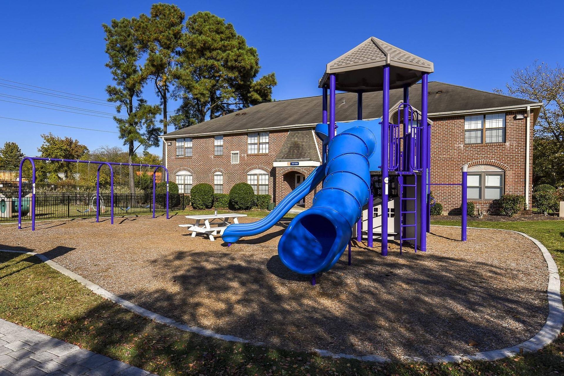 Playground with blue spiral slide and purple play structure at a brick apartment complex.