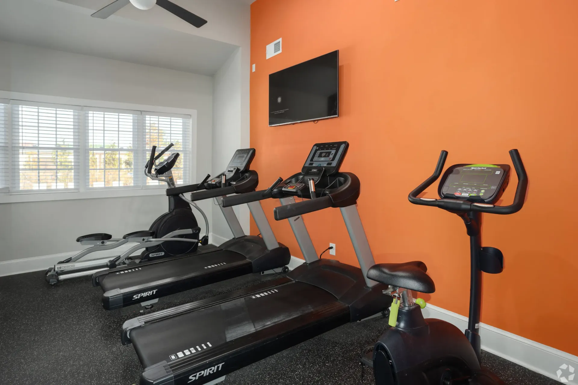 Fitness center with three treadmills and a stationary bike by an orange wall.