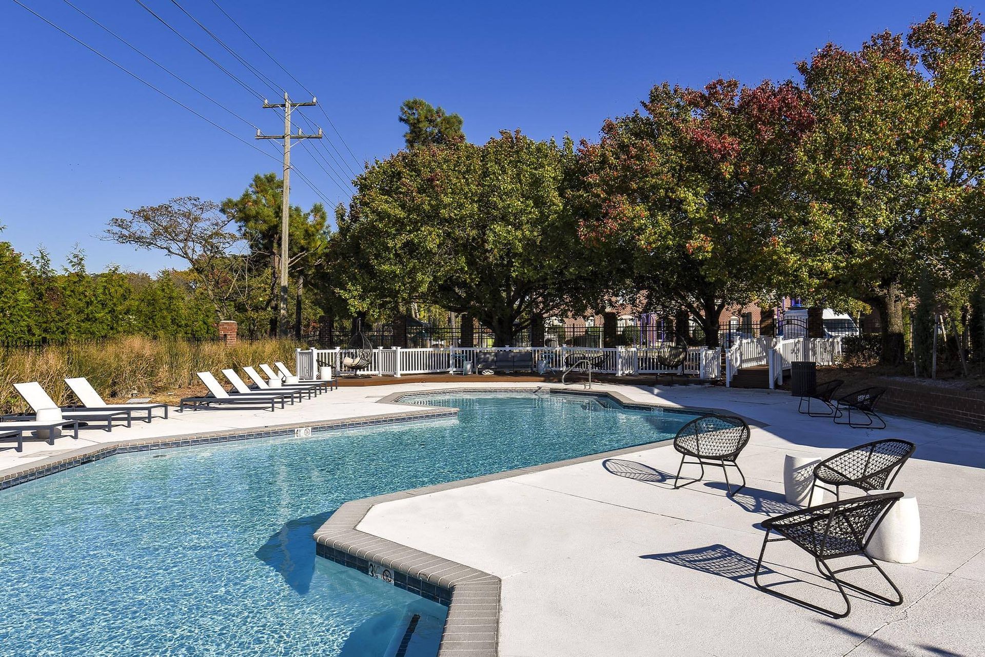 Outdoor community pool area with lounge chairs and seating under trees.