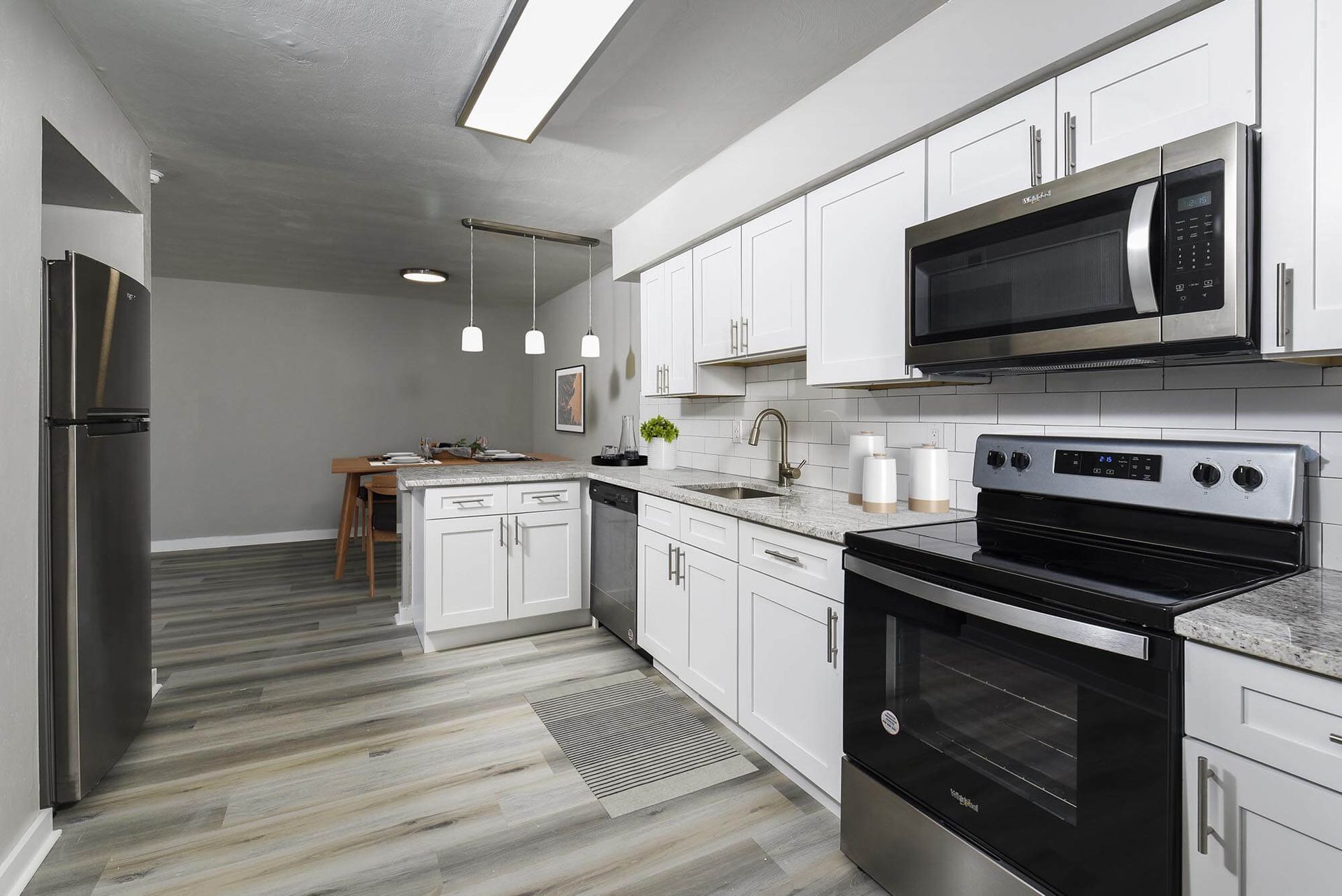 Modern kitchen with white cabinets, stainless steel appliances, and a small dining area in the background.